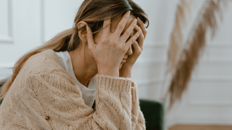 A woman holding her head in her hands, worrying and self-sabotaging.