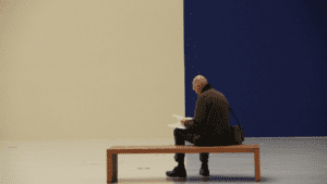A man sitting on a bench and behind him a wall painted half blue half sepia.
