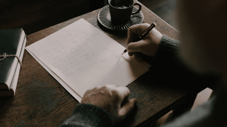 A dark background, someone writing in a notebook on a desk.