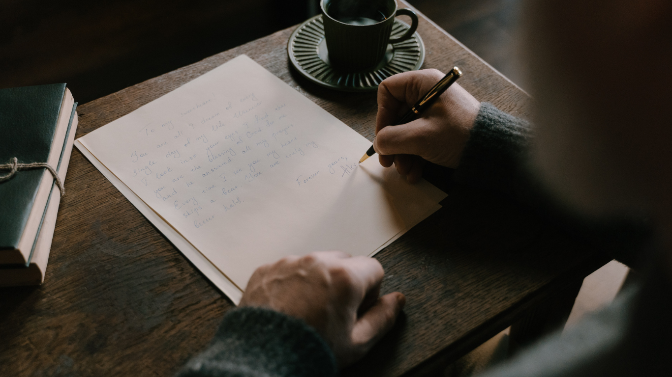 A dark background, someone writing in a notebook on a desk.