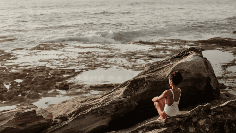 A woman meditating on a rocky structure near the sea. How to build self-esteem.